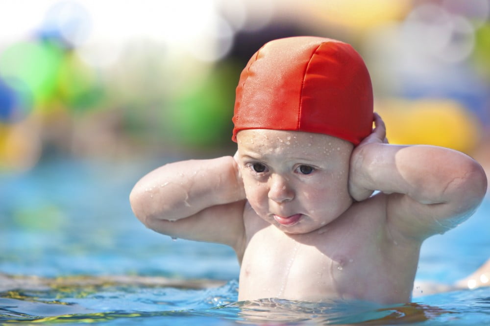 serious child with swimming pool cap hands on ears