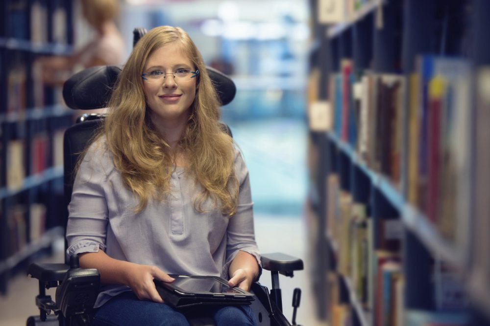 Portrait of young woman in wheelchair in library
