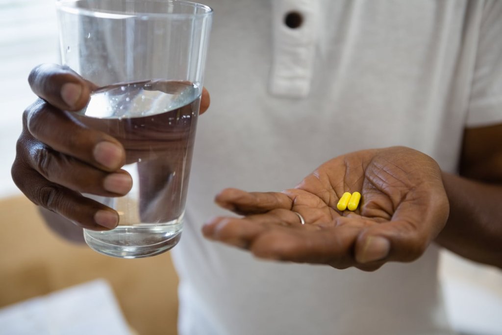 senior man holding medicines and drinking water